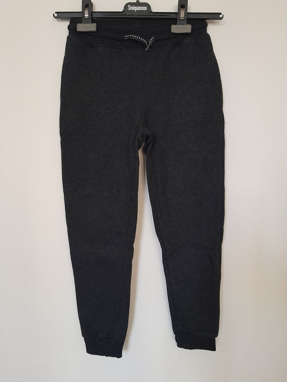 Pantalon noir pour homme, bien coupé, contre un mur blanc. Second hand.