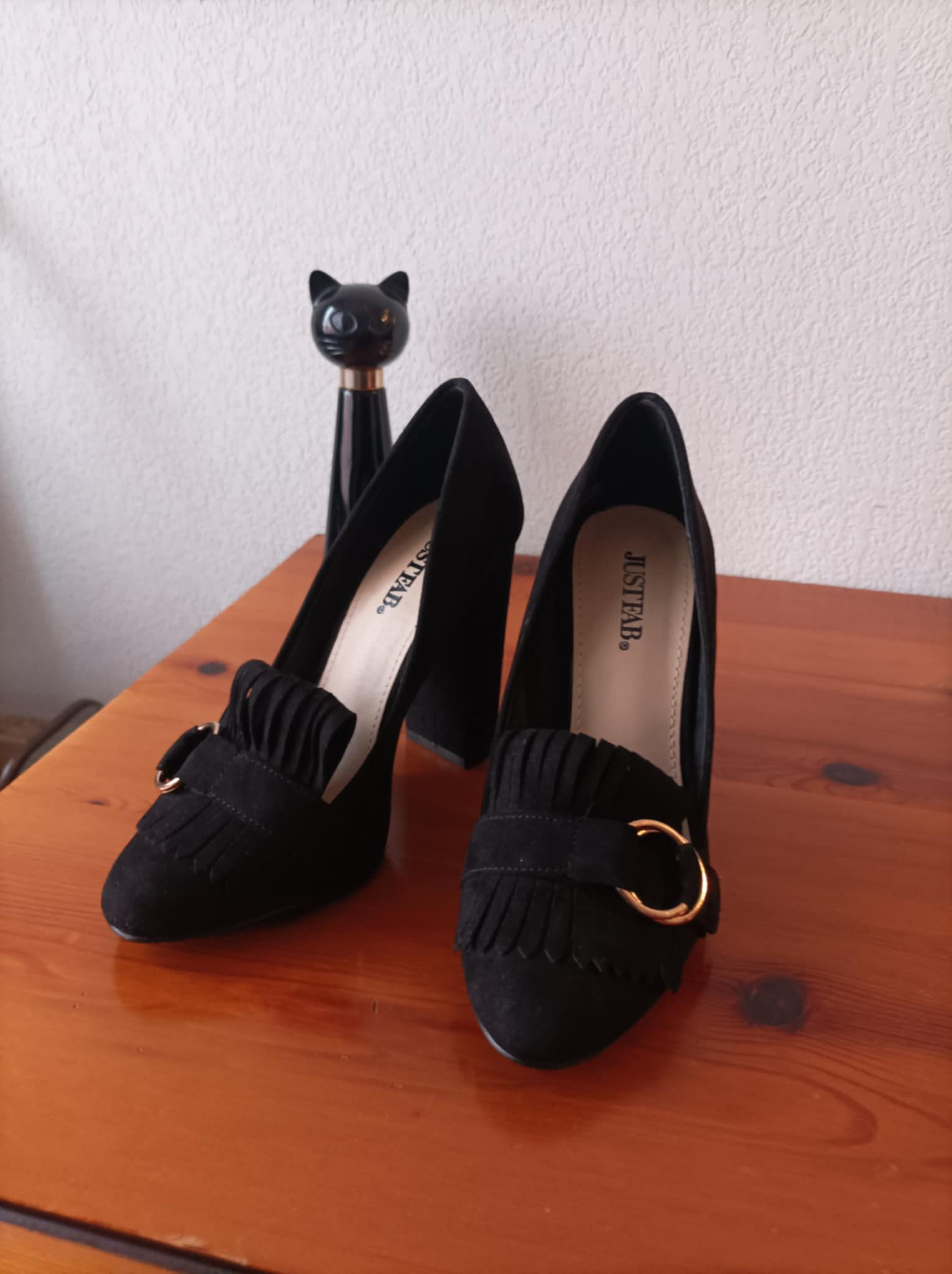 Paire de talons noirs avec boucle dorée et petits détails sur une table en bois.