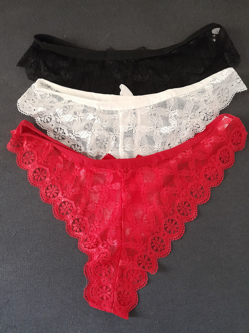 Miniature : Trois sous-vêtements en dentelle, noir, blanc et rouge, sur fond sombre.