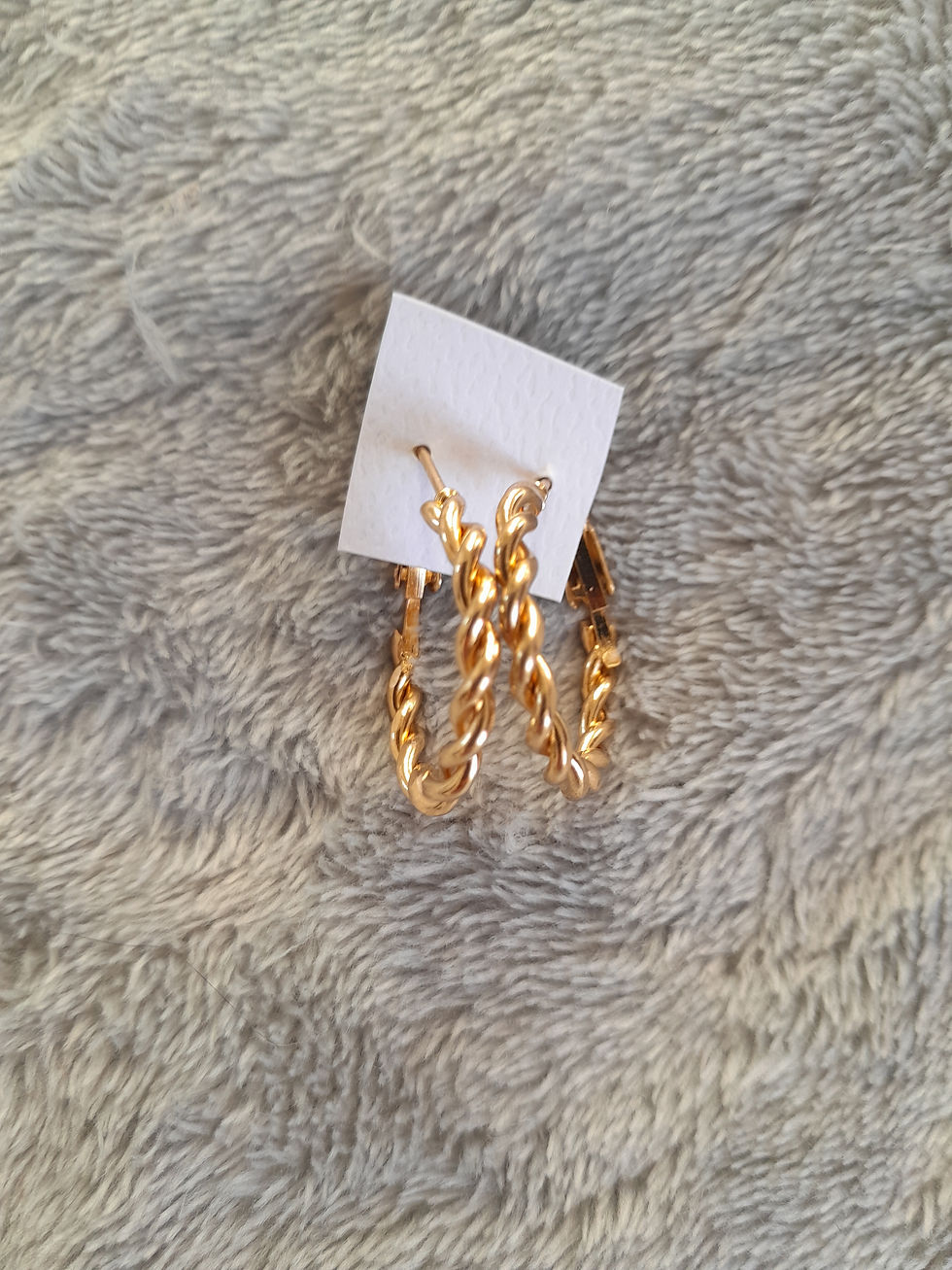 Boucles d'oreilles torsadées dorées avec une étiquette blanche sur un tissu gris.