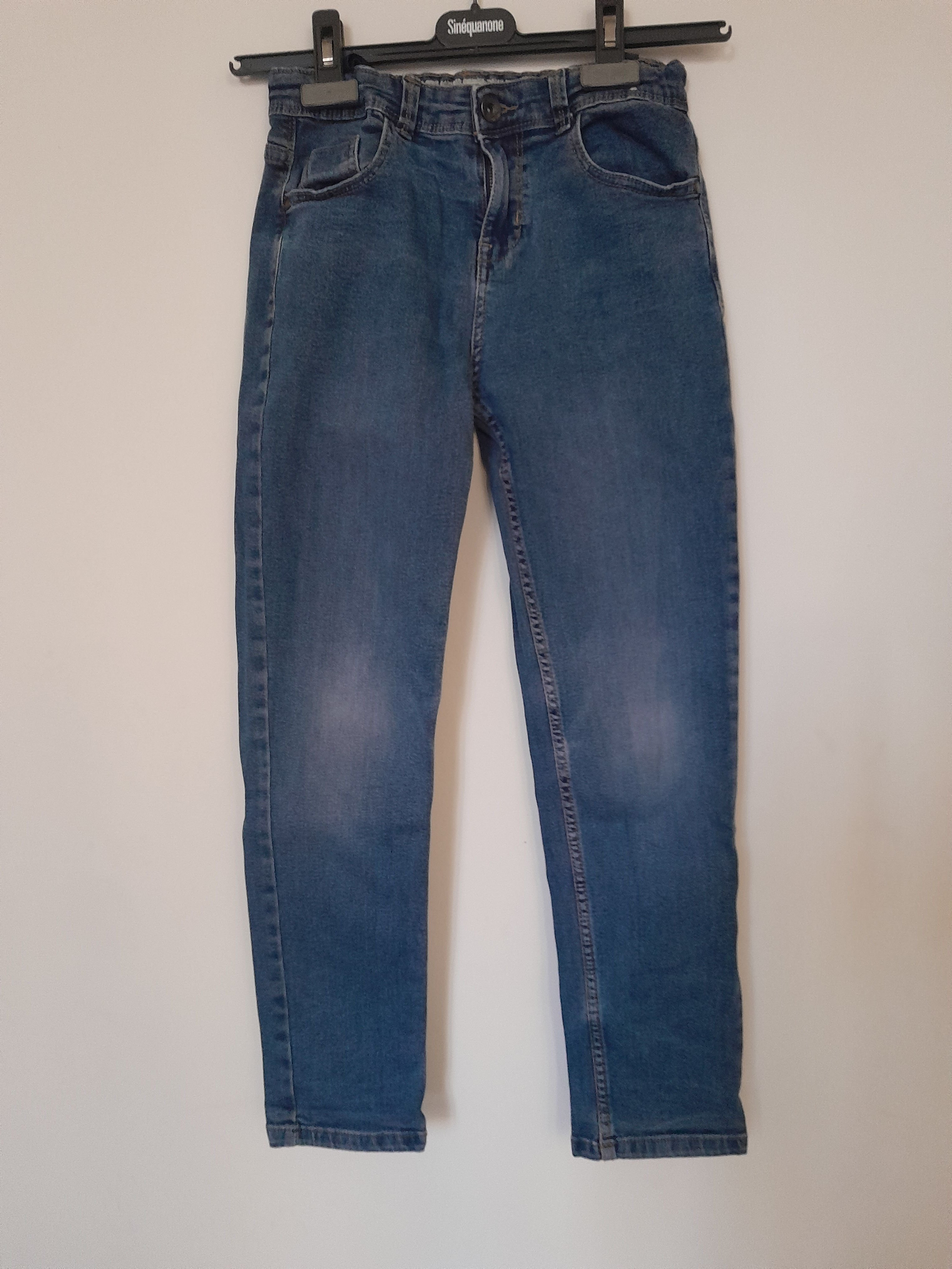 Jean bleu exposé sur un mur blanc, Pull, vue de face. Seconde Main.