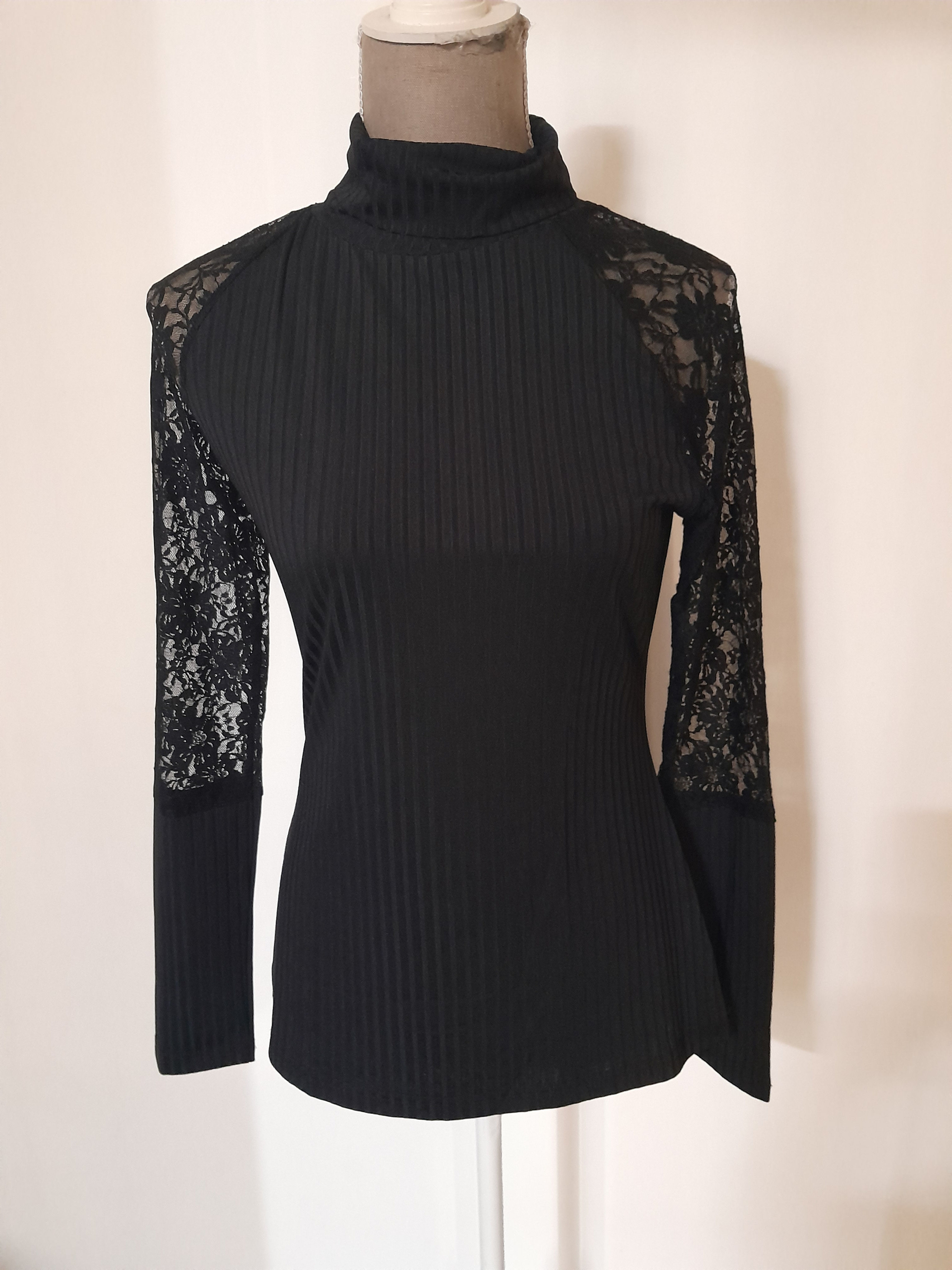 Un haut noir, col roulé et manches en dentelle, Bas, sur un fond clair.