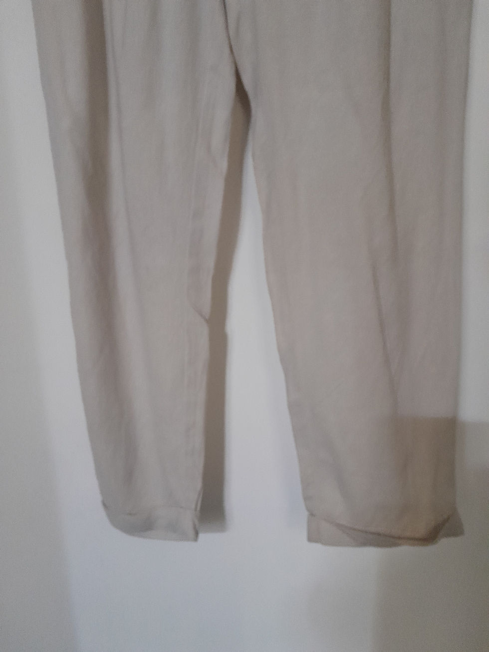 Miniature : Pantalons beiges, pliés. Le bas des pantalons, couleur crème, contre le mur, Seconde Main.