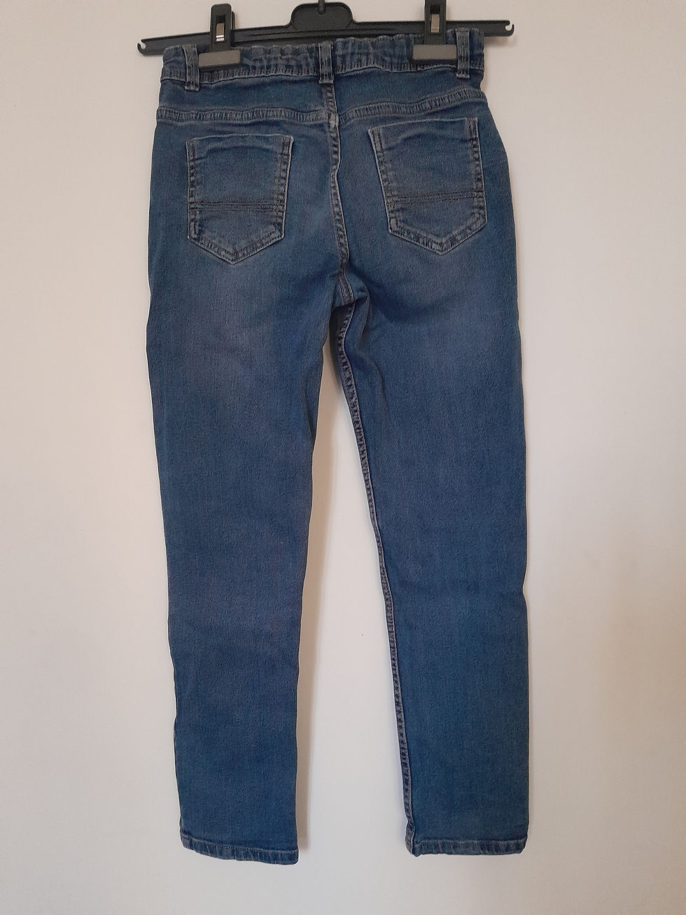 Miniature : Jeans bleus suspendus contre un mur blanc, prêt pour la vente. Seconde main.