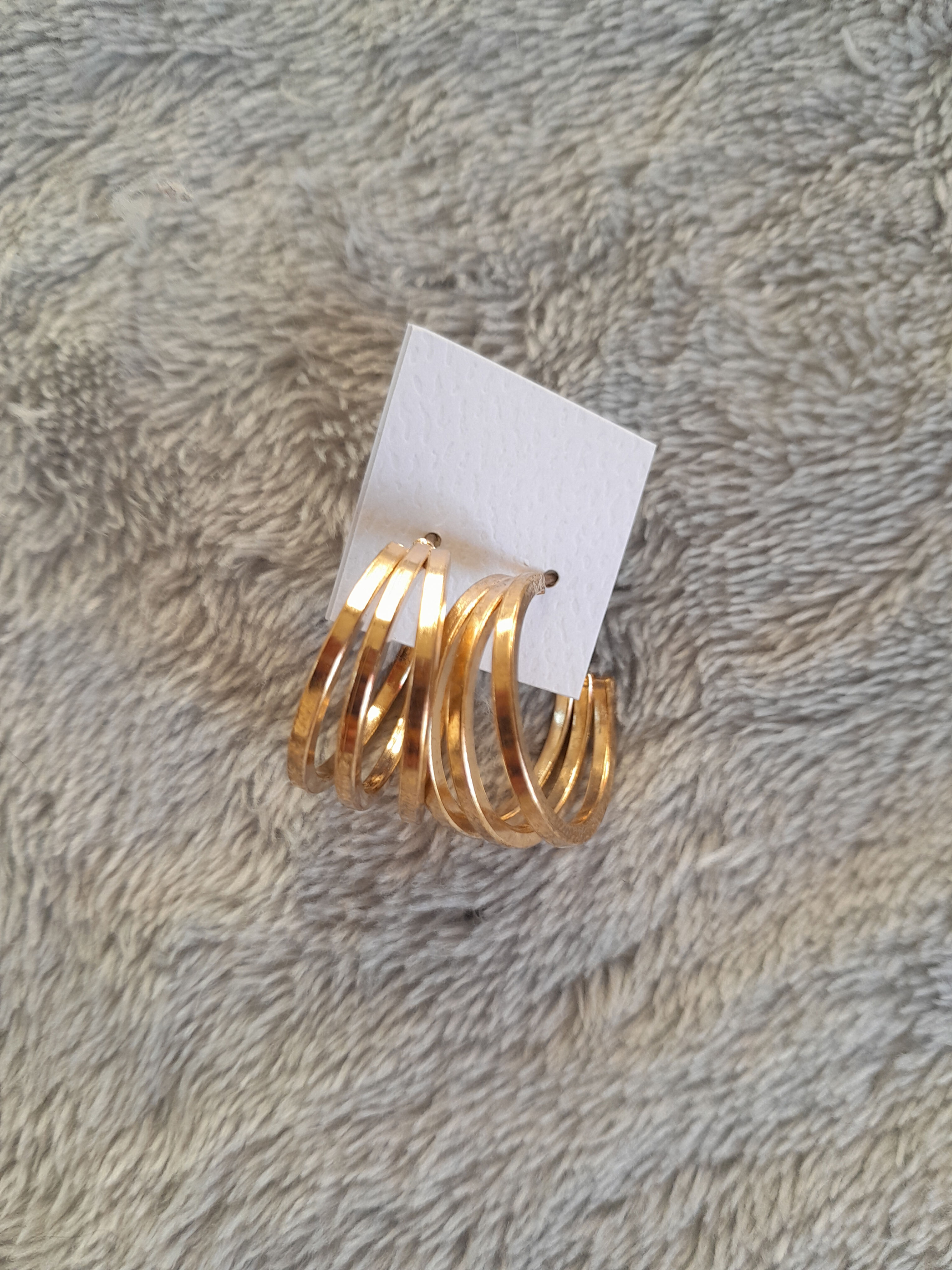 Boucles d'oreilles dorées, design à trois cercles, sur un fond texturé. Seconde Main.