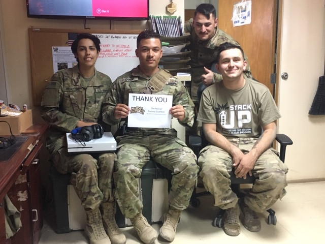 4 soldiers sit in a recreational area. They hold an xbox one s and a thank you note for the Marvel Factor Coalition.