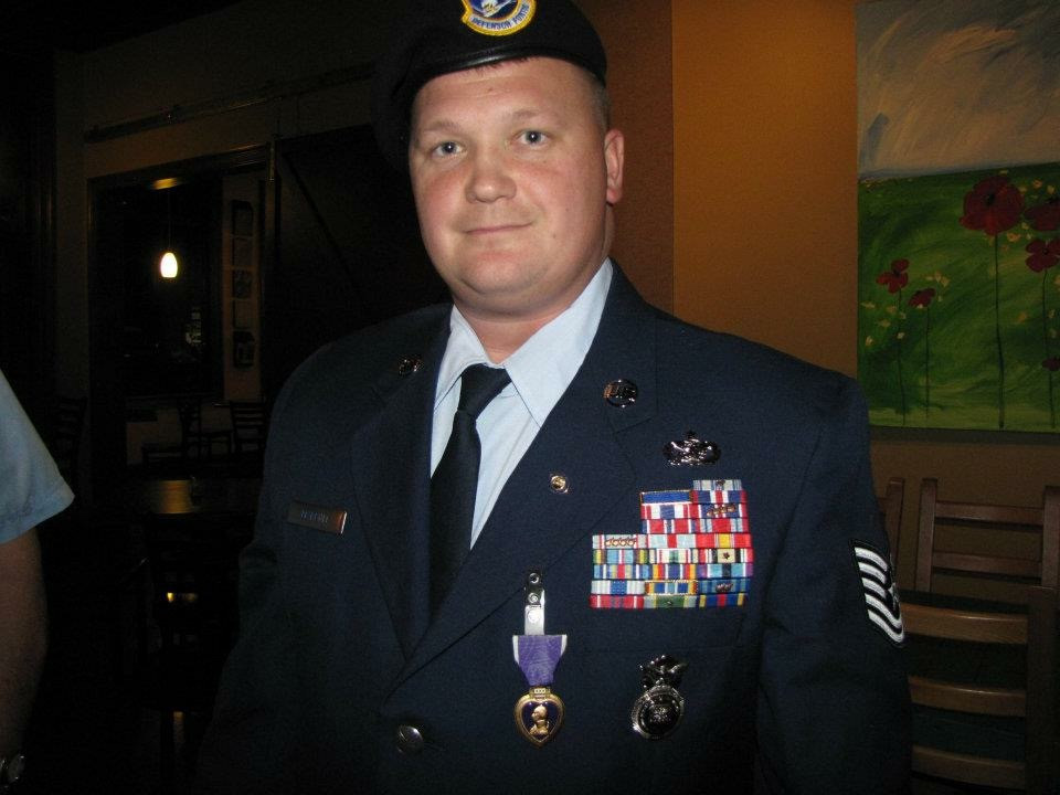 Dustin poses for a photo in full dress uniform. The left side of his chest is covered in award medals and ribbons.