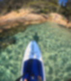 Vue depuis un paddleboard 'SROKA' sur une eau turquoise claire, avec une côte rocheuse et des arbres à Cavalière au Lavandou en arrière-plan