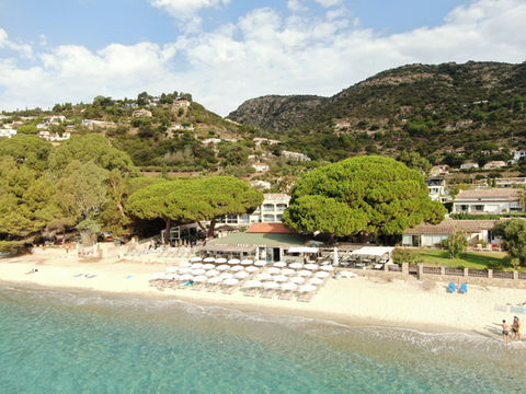 Vue aérienne d'une plage avec des parasols blancs, un restaurant et des collines en arrière-plan Pazzi Plage à Aiguebelle au Lavandou
