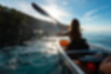 Femme pagayant dans un kayak transparent sur l'eau au lever de soleil au Lavandou