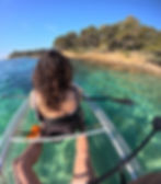 Femme pagayant dans un kayak transparent sur une eau turquoise avec une côte boisée sur la plage de Cavalière au Lavandou en arrière-plan