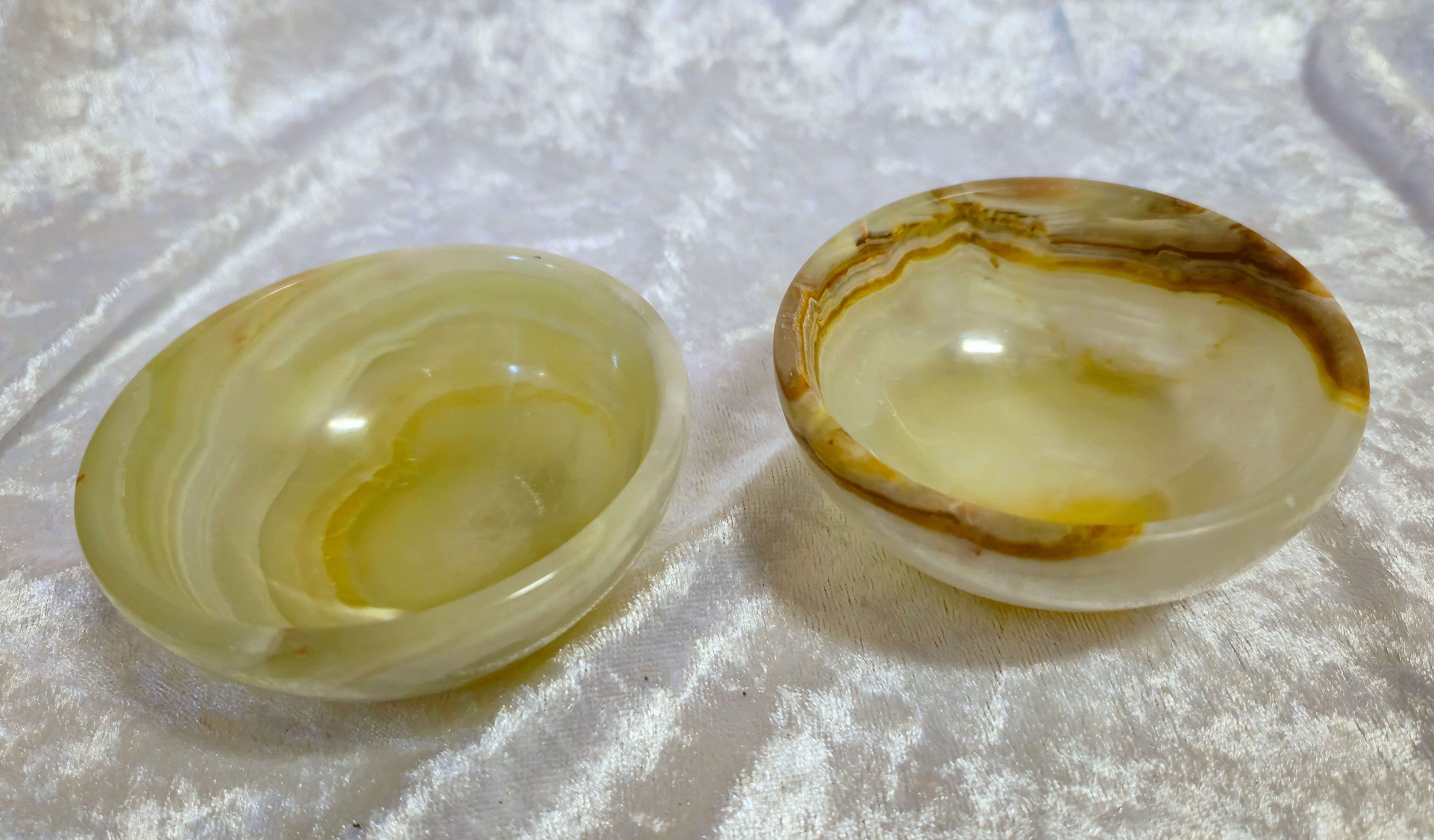 Two 3-inch banded calcite bowls with smooth, polished surfaces and natural earthy striations sit on a white velvet background