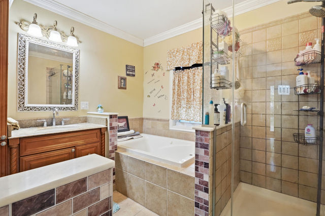 Full bathroom with tiled soaking tub, glass-enclosed shower, wood vanity, and decorative mirror.