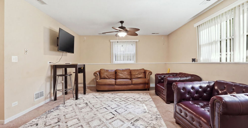 Spacious lower-level recreation room with carpet flooring, seating, and a bar table.