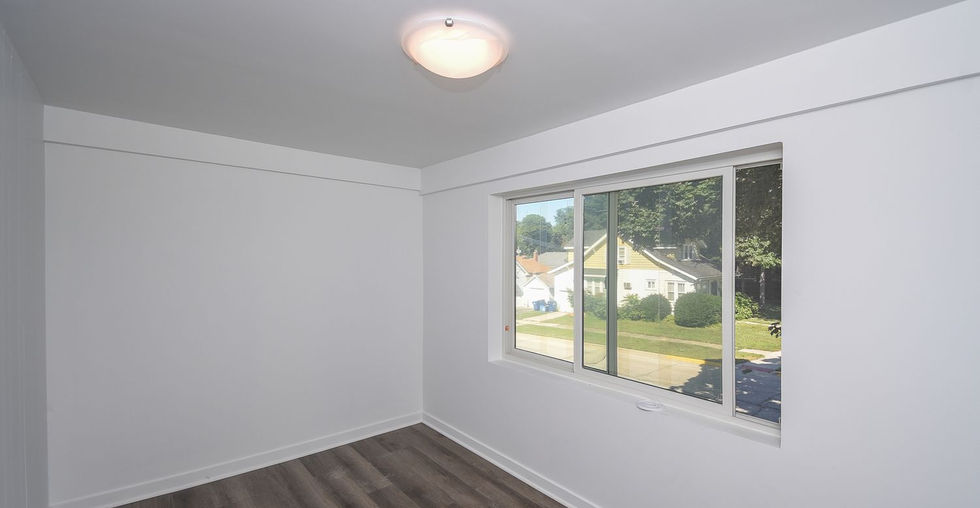 Bright bedroom with modern flooring, neutral walls, and a wide window overlooking the neighborhood