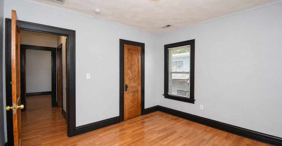 Bedroom with wood-look flooring, natural wood doors, black trim, and a large window
