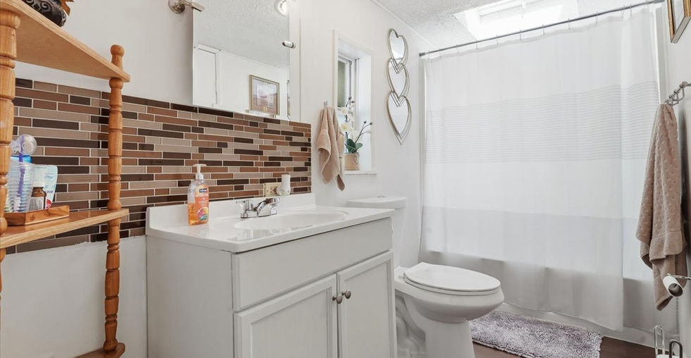 Second bathroom with white vanity, decorative backsplash, toilet, shower curtain, skylight, and wood-style flooring.