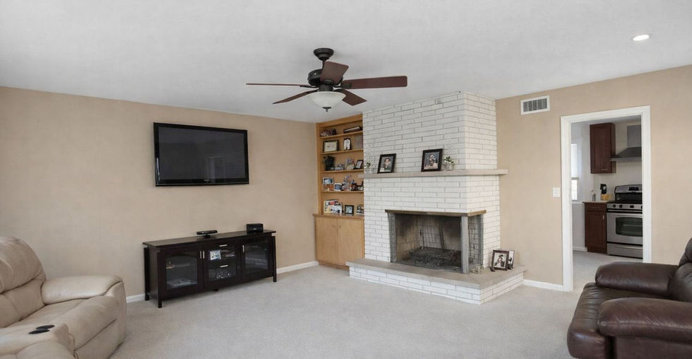 Spacious living room at 2204 Edgewood Rd in Waukegan, IL, with light carpet, white brick fireplace, built-in shelving, and wall-mounted TV.