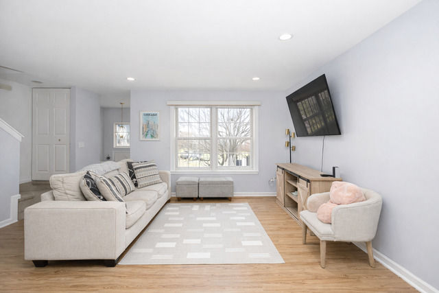 Bright living room with large front window, light wood flooring, mounted TV, and neutral seating