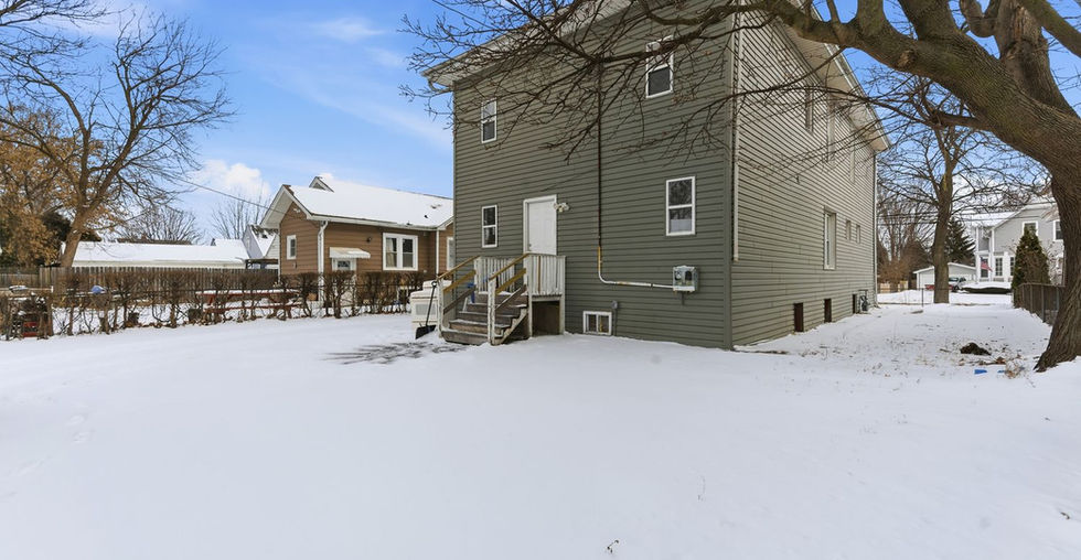 Backyard view of home with wide snowy yard and neighboring houses