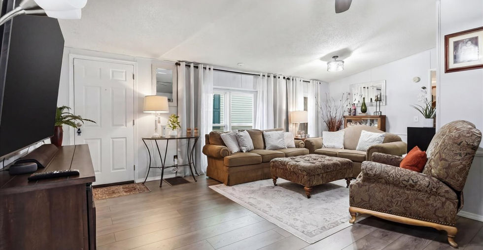 Living room with wood-style flooring, neutral walls, large windows, sofa seating, accent chairs, and ceiling fan lighting.