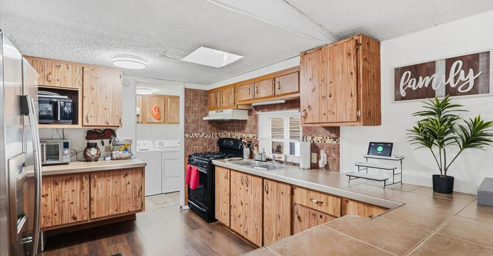 Kitchen with wood cabinetry, tiled countertops, gas stove, stainless steel refrigerator, and open layout.