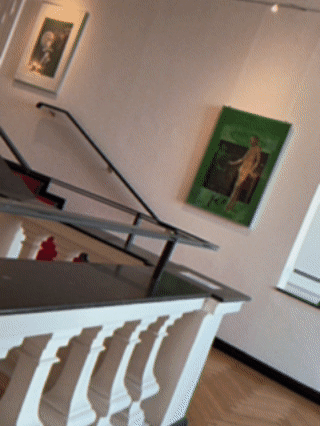 Schräg gefilmtes Treppenhaus in den Räumlichkeiten des Sozialgerichts Oldenburg mit weißen Wänden, schwarzem Geländer, gerahmten Bildern und grünem Gemälde.