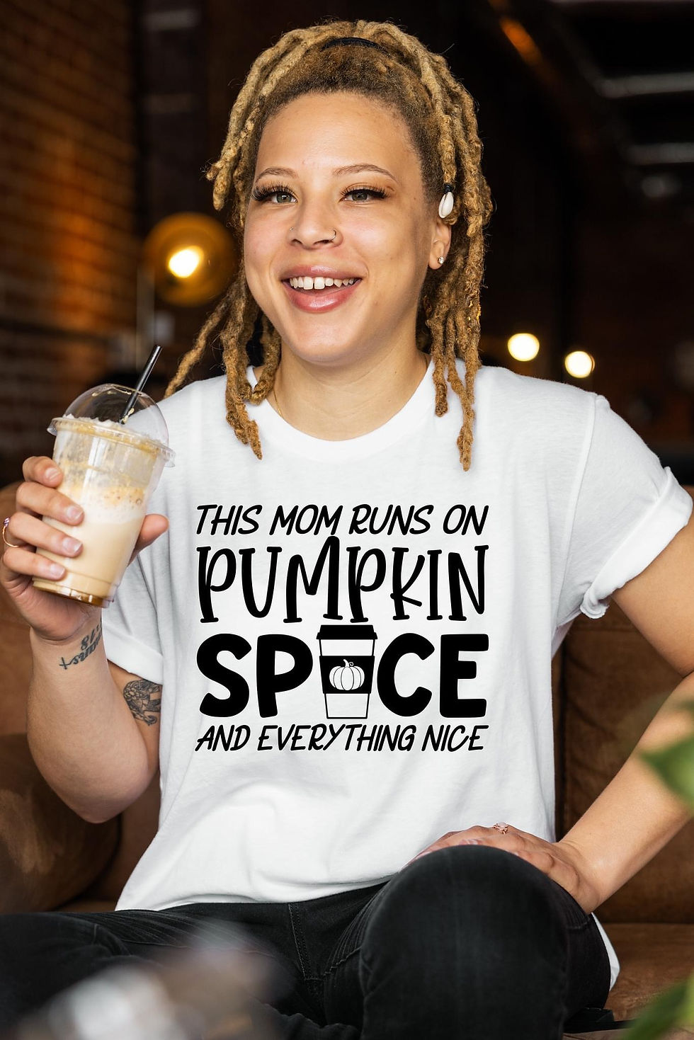 Woman wearing a white shirt with the phrase "This Nurse Runs on Pumpkin Spice and Everything Nice" and a pumpkin spice coffee