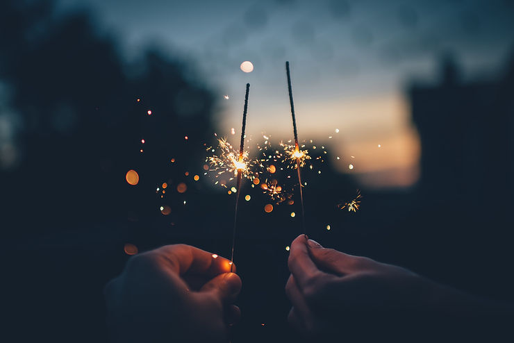 A photo of two hands holding sparklers in an evening