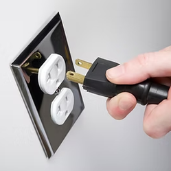 Close-up photo of a hand plugging in an electrical cord to an outlet.