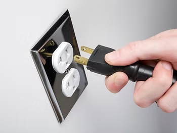 Close-up photo of a hand plugging in an electrical cord to an outlet.