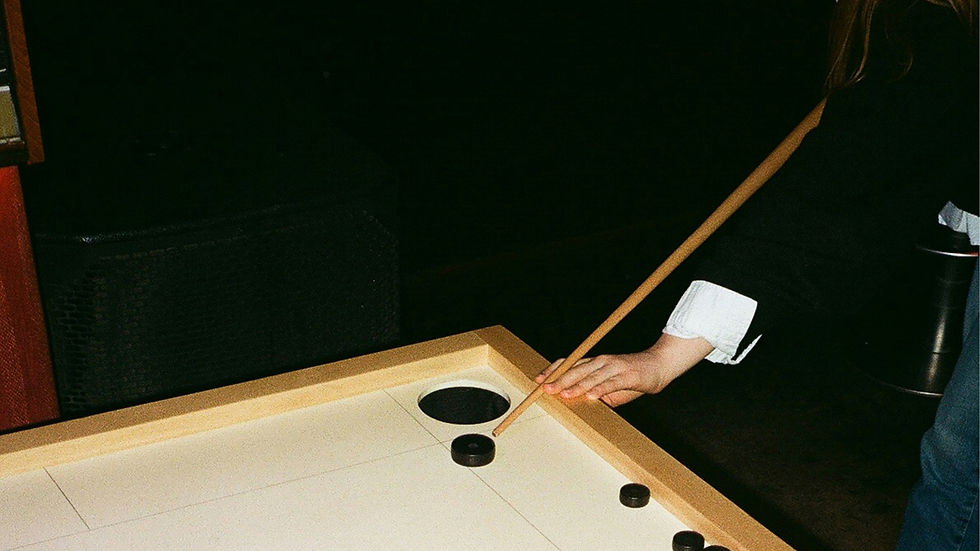 Person playing air hockey, holding a brown cue near a puck on a white table. Background is dark, conveying a focused mood.