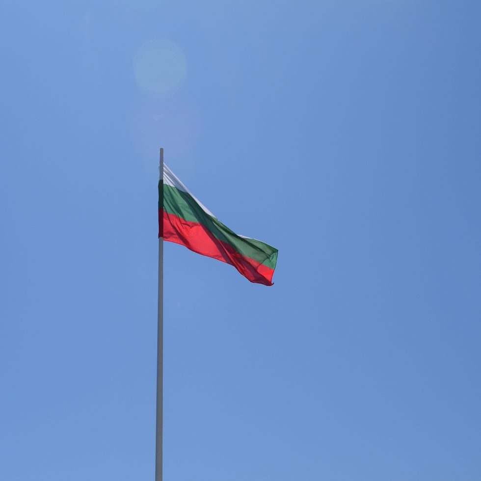Bulgarian flag with white, green, and red stripes waves against a clear blue sky, creating a serene and patriotic scene.