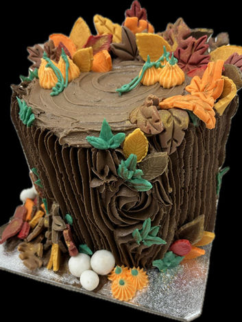 Autumnal buttercream celebration cake shaped like a tree log, decorated with handmade leaves and mushrooms — perfect for seasonal events.