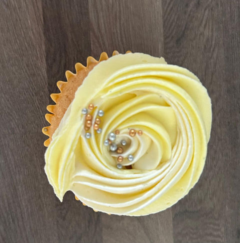 Homemade cupcake topped with yellow buttercream swirls and finished with silver and gold edible pearls.