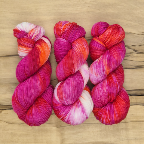 Three skeins of bright pink, orange and white sock yarn.