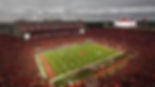 Memorial Stadium: A packed Memorial Stadium in Lincoln, Nebraska, with fans cheering during a Nebraska Cornhuskers football game under an overcast sky.