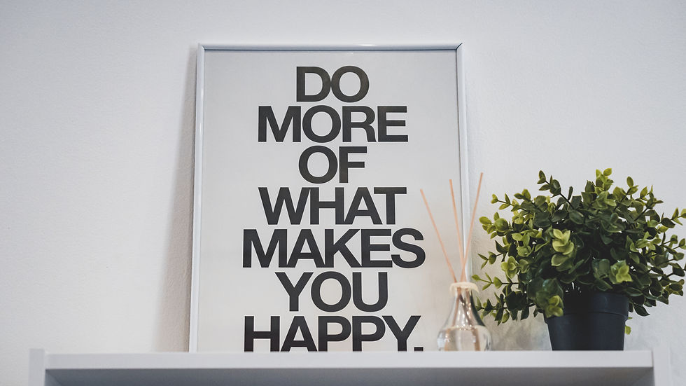 Framed quote "Do more of what makes you happy" on a white wall. Shelf below holds a green plant and reed diffuser, creating a calm vibe.