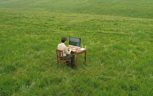 Man sitting in grassy field with desk and computer