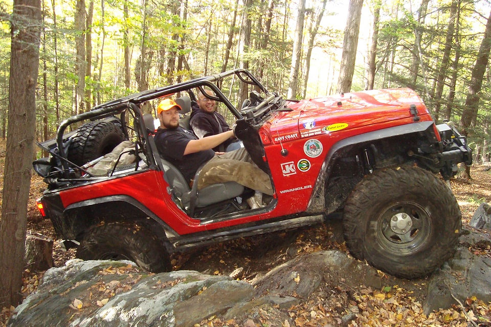 Two men in a red Jeep tackling a rocky trail