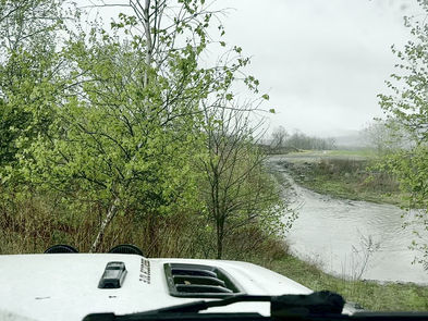 Jeep crossing a pond with a large splash of muddy water coming over the hood and hitting the windshield