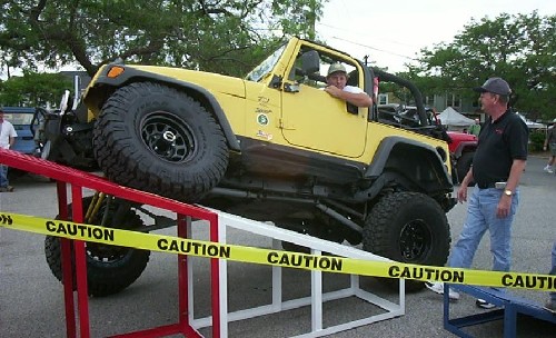 Man in yellow Jeep ascending ramp; Caution tape visible