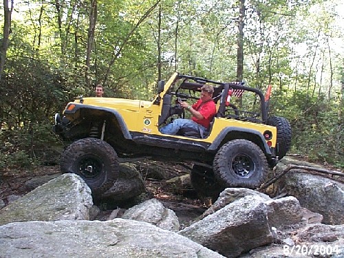 Man driving yellow Jeep over rocks