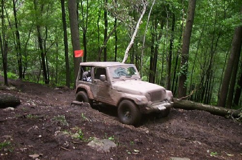 Muddy Jeep traversing wooded trail