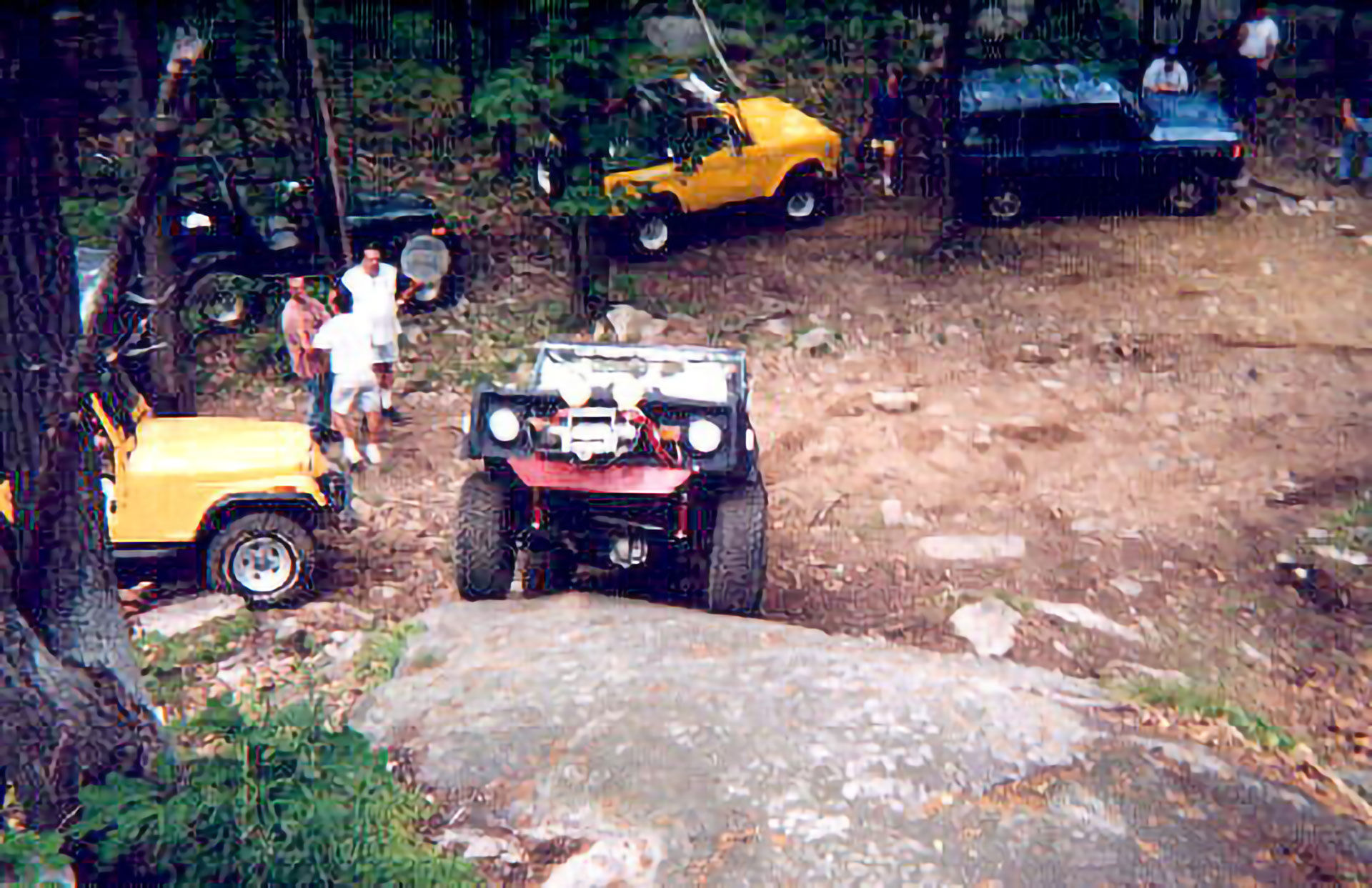 Jeep navigating rocky terrain, off-road enthusiasts watching