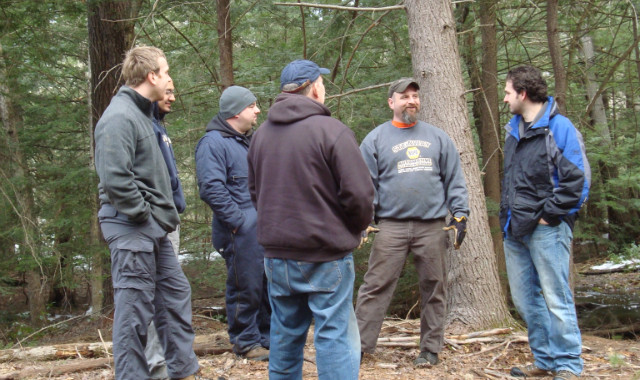 Five men converse in a wooded area