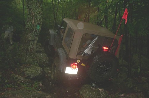 Tan Jeep traversing rocky, wooded trail