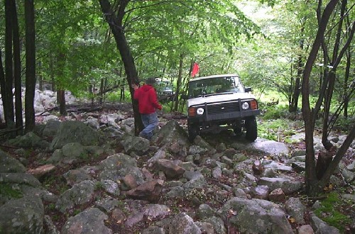 Person guiding white Land Rover over rocks