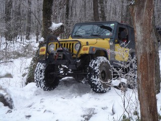Yellow Jeep traversing snowy, wooded terrain
