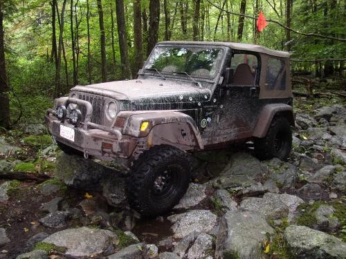 Muddy Jeep Wrangler traversing rocky terrain